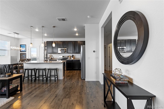 kitchen with dark wood-style flooring, a kitchen breakfast bar, visible vents, appliances with stainless steel finishes, and hanging light fixtures