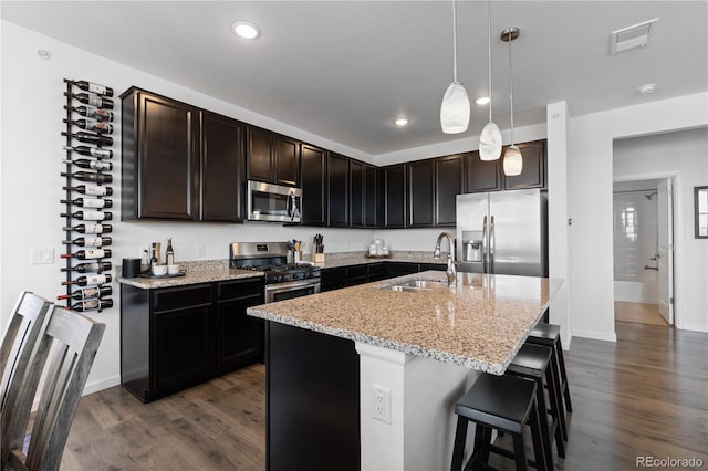 kitchen with light stone counters, dark wood-style floors, a kitchen bar, appliances with stainless steel finishes, and a sink