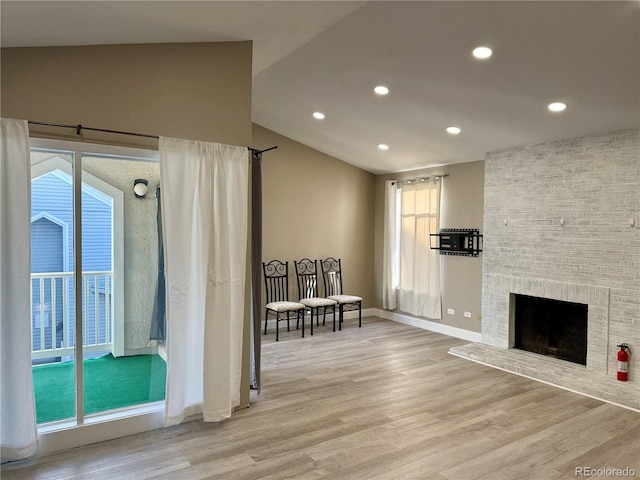 unfurnished room featuring a fireplace, light hardwood / wood-style floors, lofted ceiling, and a wealth of natural light