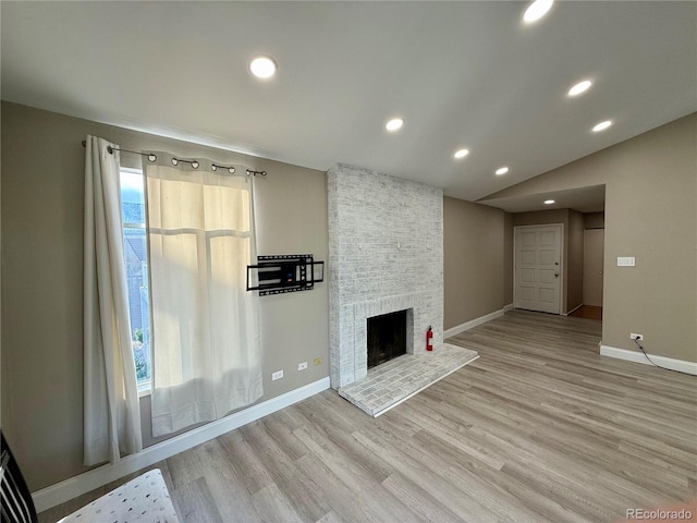 unfurnished living room featuring a fireplace, vaulted ceiling, and light wood-type flooring