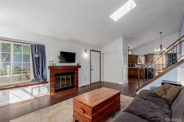 living area featuring stairway, an inviting chandelier, vaulted ceiling with skylight, a fireplace, and hardwood / wood-style flooring