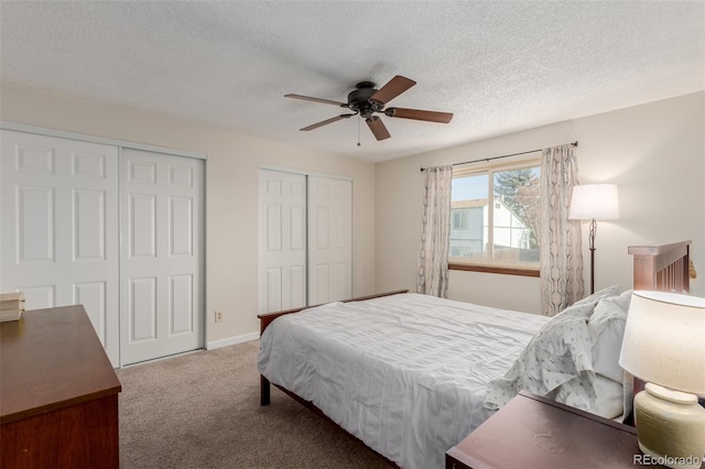 bedroom with two closets, baseboards, carpet, a textured ceiling, and a ceiling fan