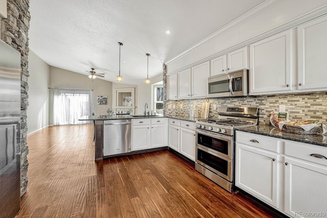 kitchen featuring backsplash, stainless steel appliances, vaulted ceiling, decorative light fixtures, and white cabinets