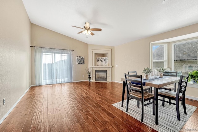 dining room with wood-type flooring, ceiling fan, lofted ceiling, and a tiled fireplace