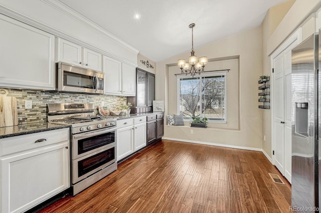 kitchen with appliances with stainless steel finishes, backsplash, an inviting chandelier, dark stone countertops, and white cabinetry