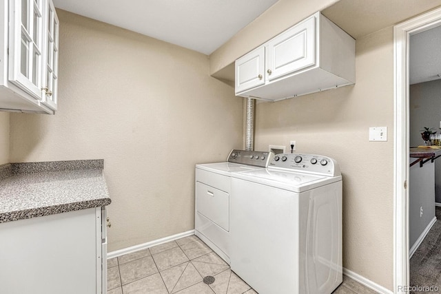 laundry area featuring separate washer and dryer, light tile patterned floors, and cabinets