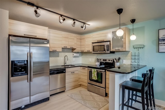 kitchen featuring a breakfast bar area, stainless steel appliances, a sink, hanging light fixtures, and tasteful backsplash