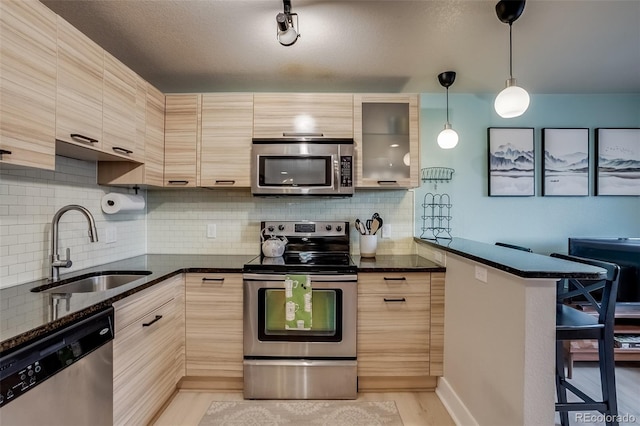 kitchen featuring dark stone counters, appliances with stainless steel finishes, a kitchen breakfast bar, a sink, and backsplash