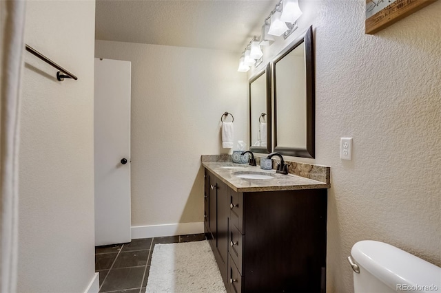 bathroom with baseboards, double vanity, a sink, and tile patterned floors