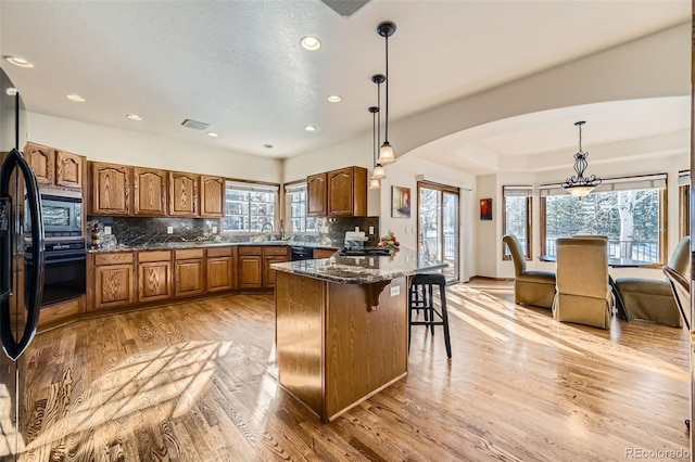 kitchen featuring decorative light fixtures, light hardwood / wood-style flooring, black appliances, and a kitchen island