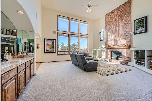 carpeted living room with a brick fireplace, ceiling fan, and a high ceiling