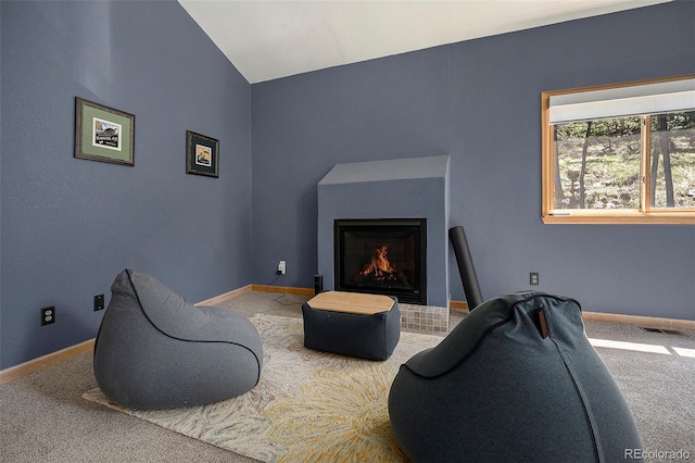 carpeted living room featuring a lit fireplace, baseboards, and vaulted ceiling