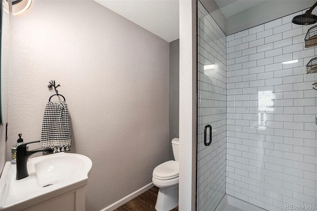 bathroom featuring wood finished floors, a shower stall, toilet, a sink, and baseboards