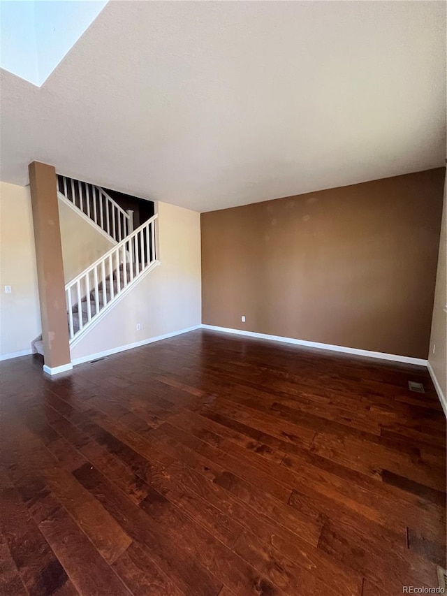 unfurnished living room featuring dark wood-type flooring and a skylight