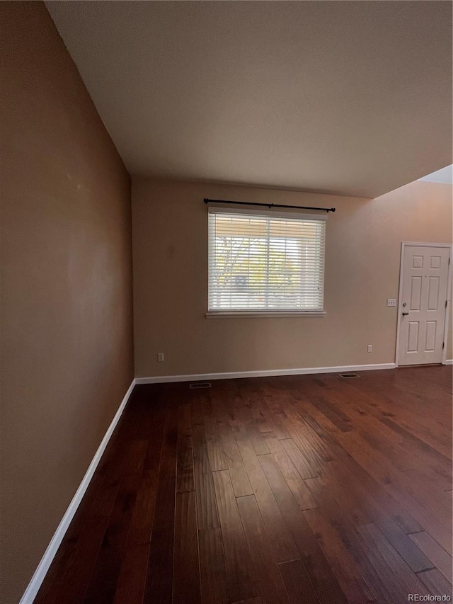 spare room with dark wood-type flooring and lofted ceiling