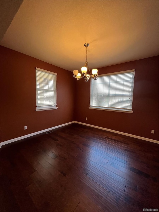 empty room with dark wood-type flooring and an inviting chandelier