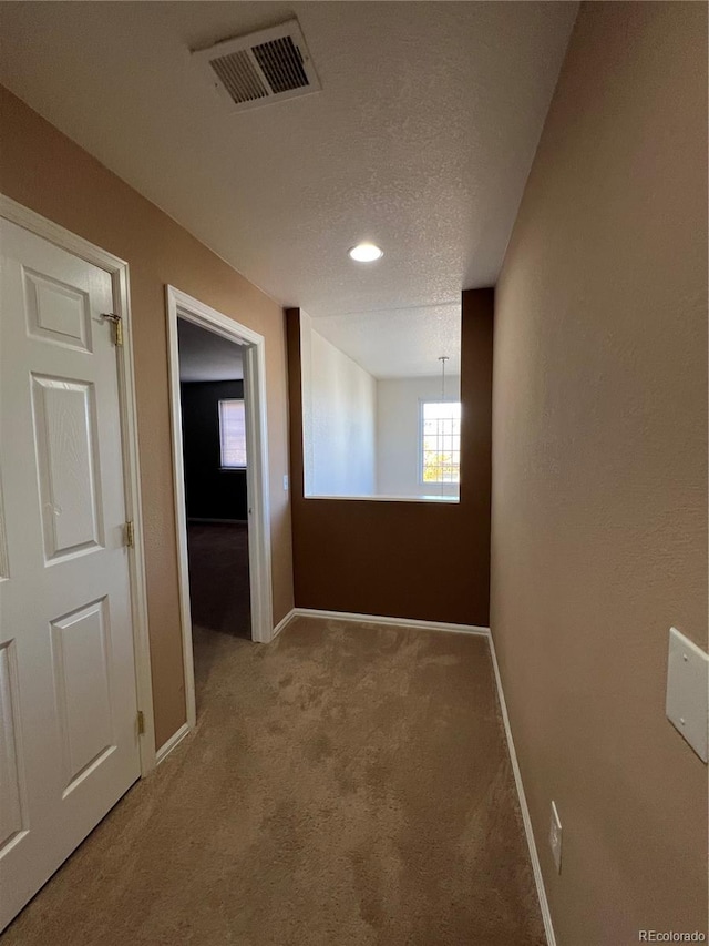 corridor with a textured ceiling and carpet flooring