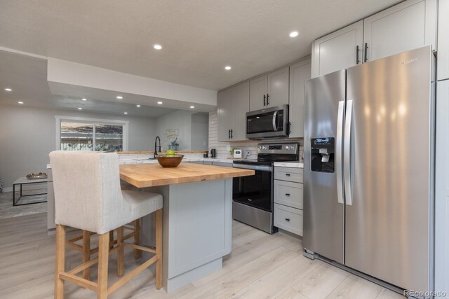 kitchen with butcher block counters, a center island, appliances with stainless steel finishes, a kitchen breakfast bar, and backsplash