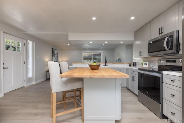 kitchen with a kitchen bar, butcher block counters, sink, a center island, and appliances with stainless steel finishes