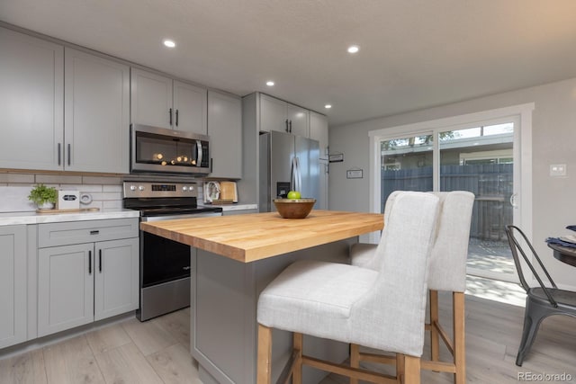 kitchen featuring appliances with stainless steel finishes, a breakfast bar, butcher block countertops, tasteful backsplash, and gray cabinetry