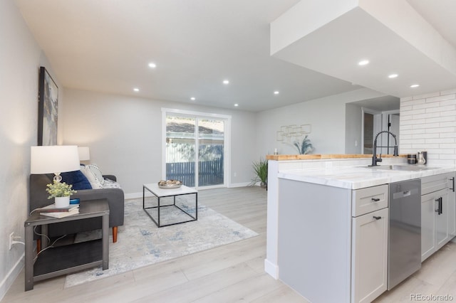 kitchen featuring sink, white cabinetry, light stone counters, stainless steel dishwasher, and light hardwood / wood-style floors