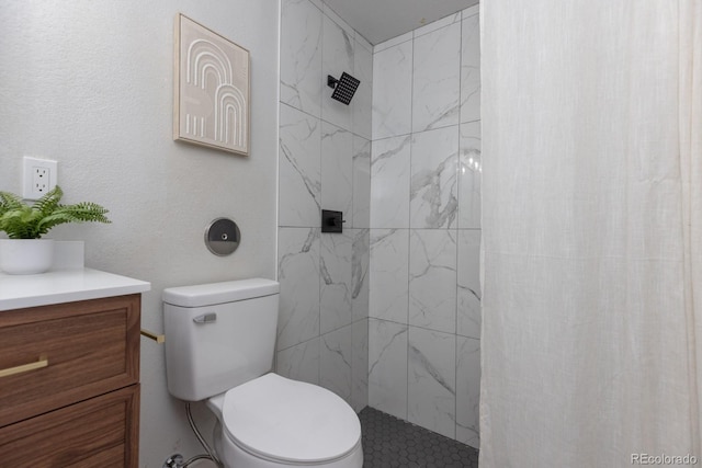 bathroom featuring vanity, a tile shower, and toilet