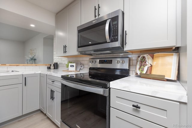 kitchen with tasteful backsplash, white cabinetry, appliances with stainless steel finishes, and light hardwood / wood-style flooring