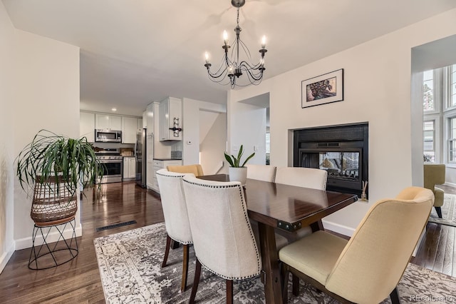 dining area with a chandelier, dark wood-style floors, a multi sided fireplace, and baseboards