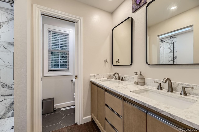 bathroom with double vanity, a marble finish shower, and baseboards