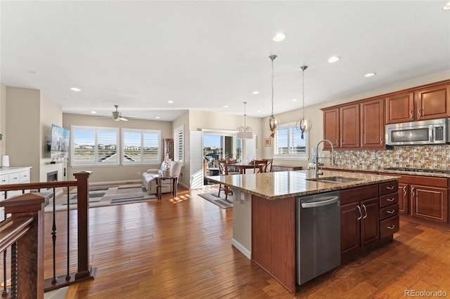 3278 Ghost Dance Dr, Castle Rock, CO 80108 - kitchen featuring appliances with stainless steel finishes, an island with sink, open floor plan, light stone counters, and dark wood-style flooring