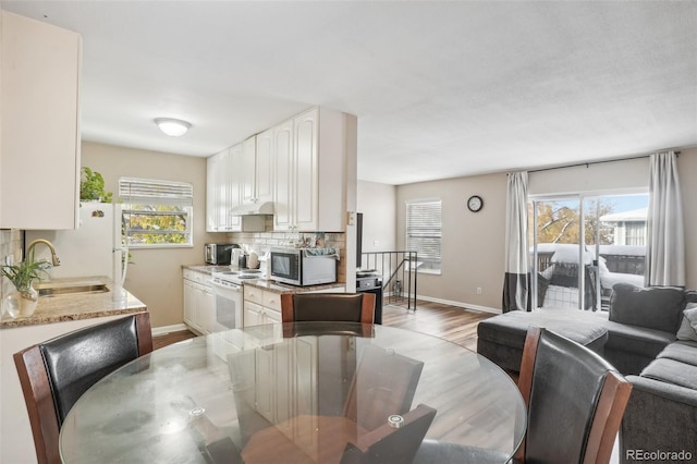 kitchen with white appliances, sink, decorative backsplash, light hardwood / wood-style floors, and white cabinetry