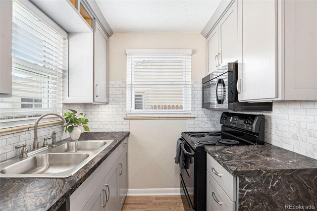 kitchen with black appliances, a sink, backsplash, light wood-style flooring, and baseboards