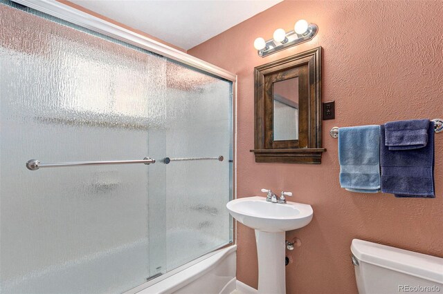 bathroom featuring toilet, enclosed tub / shower combo, and a sink