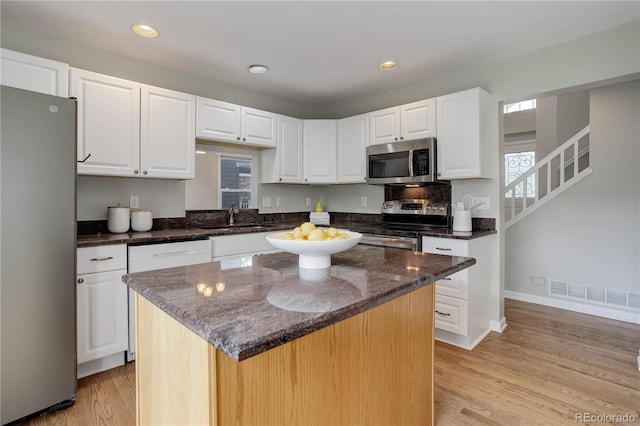 8652 Aberdeen Cir, Highlands Ranch, CO 80130 - kitchen with appliances with stainless steel finishes, white cabinetry, light wood finished floors, dark stone counters, and recessed lighting