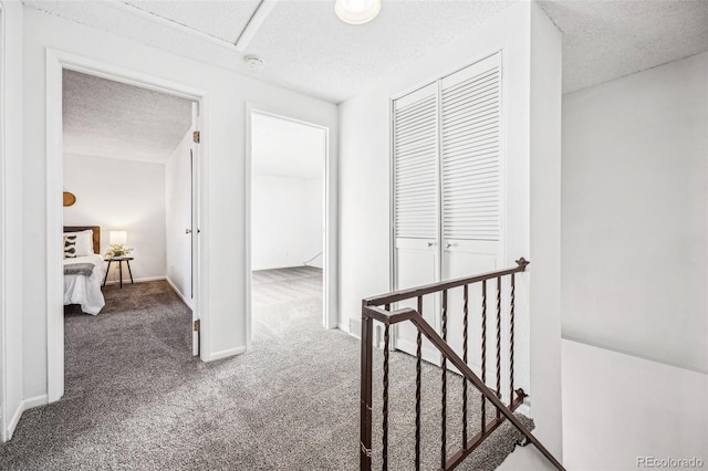 corridor with a textured ceiling, carpet floors, an upstairs landing, and baseboards