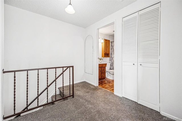 interior space with a closet, a textured ceiling, baseboards, and ensuite bathroom