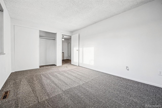 unfurnished bedroom with visible vents, arched walkways, carpet, a textured ceiling, and a closet