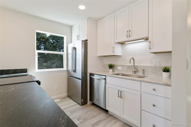 kitchen with stone counters, white cabinets, sink, light hardwood / wood-style floors, and stainless steel appliances