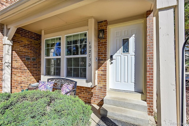 doorway to property with covered porch and brick siding