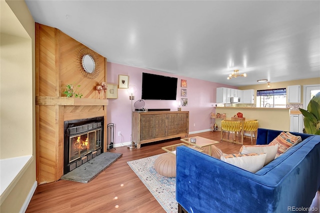 living area with a glass covered fireplace, baseboards, and wood finished floors