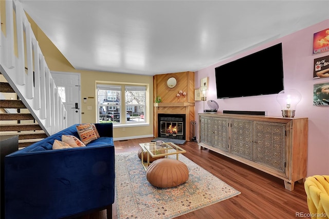 living area featuring a fireplace, stairs, and wood finished floors