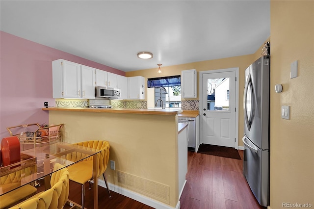 kitchen featuring white cabinets, appliances with stainless steel finishes, a sink, a peninsula, and dark wood-style floors