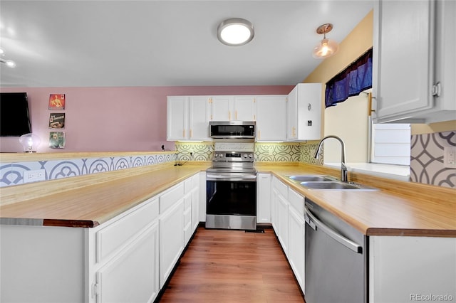 kitchen with appliances with stainless steel finishes, a sink, light countertops, a peninsula, and backsplash