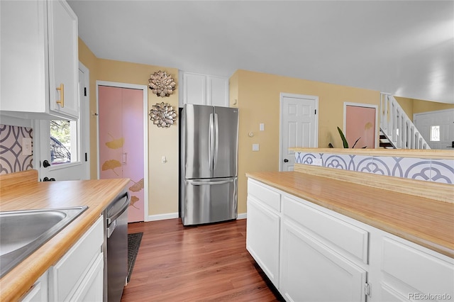 kitchen with appliances with stainless steel finishes, dark wood finished floors, a sink, baseboards, and white cabinetry