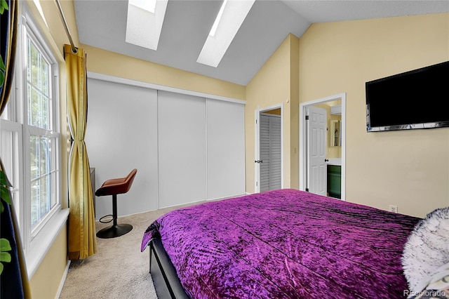 carpeted bedroom featuring a closet, connected bathroom, and vaulted ceiling with skylight