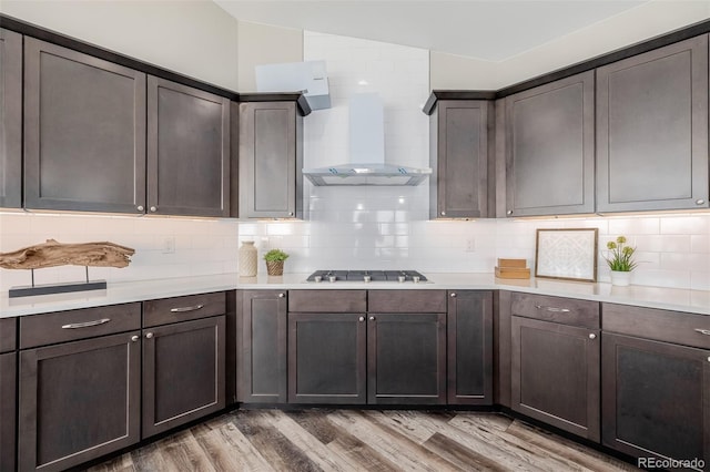 kitchen with wood-type flooring, dark brown cabinets, decorative backsplash, and wall chimney exhaust hood