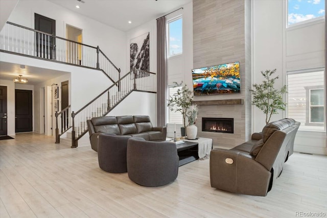 living area with a high ceiling, stairway, healthy amount of natural light, wood finished floors, and a tiled fireplace