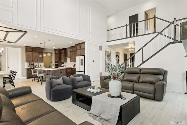 living area featuring a high ceiling, light wood-type flooring, stairway, a chandelier, and baseboards