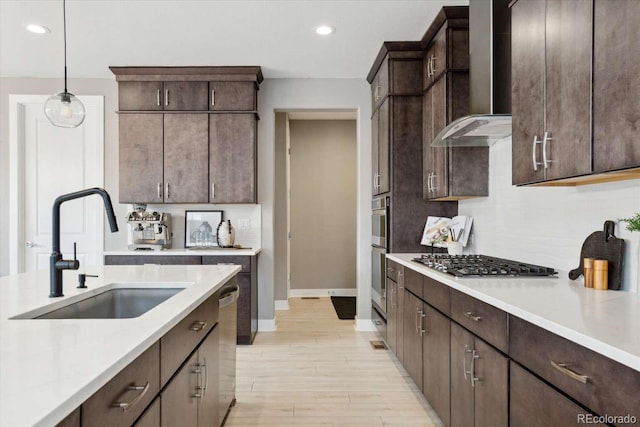 kitchen with stainless steel appliances, wall chimney exhaust hood, a sink, baseboards, and dark brown cabinetry