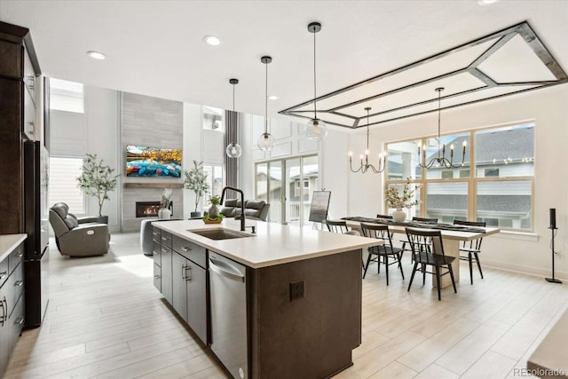 kitchen with a sink, a tile fireplace, light countertops, dishwasher, and dark brown cabinetry